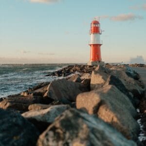 A red and white lighthouse sitting on top of a rocky shore